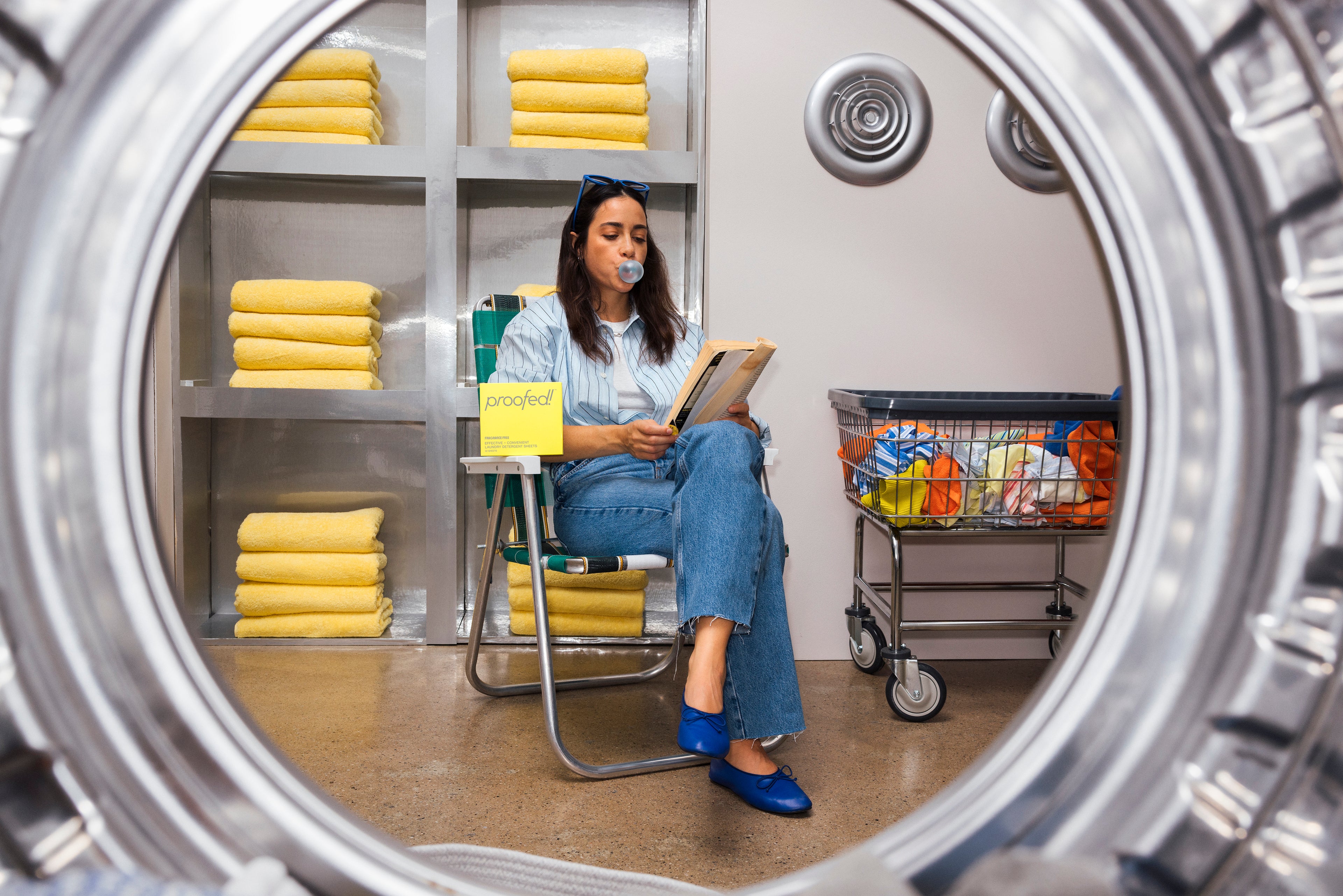Girl in blue shirt and jeans popping blue bubble gum while reading a book and waiting for her laundry