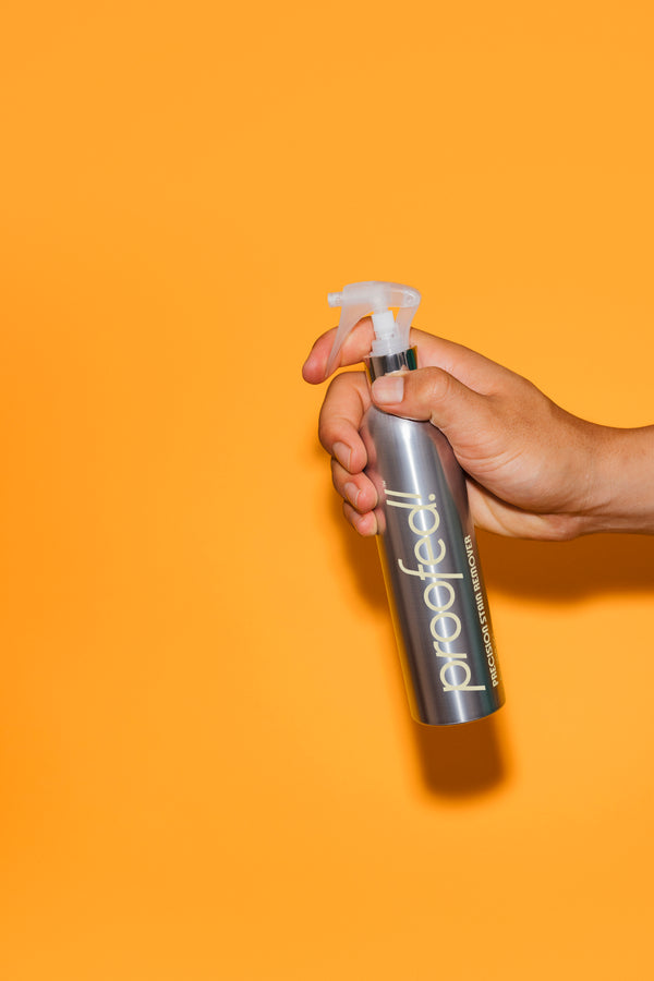 Hand spraying Proofed Precision Stain Remover Silver bottle with white spray nozzle on orange background